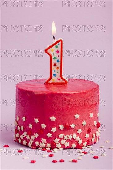 Lighted number one candle red cake with star sprinkles against purple backdrop