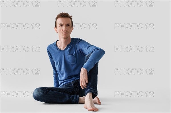 Portrait of middle aged man in blue longsleeve and jeans sitting on the floor with bare feet
