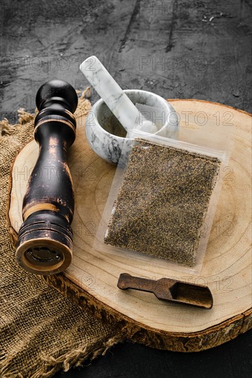 Wooden cross section with mustard in plastic package and stone mortar and mill