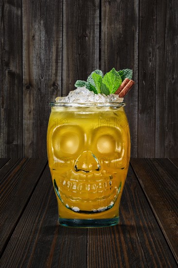 Halloween cocktail in goblet skull on wooden shelf. Jolly Roger drink in glass cup in the shape of skull