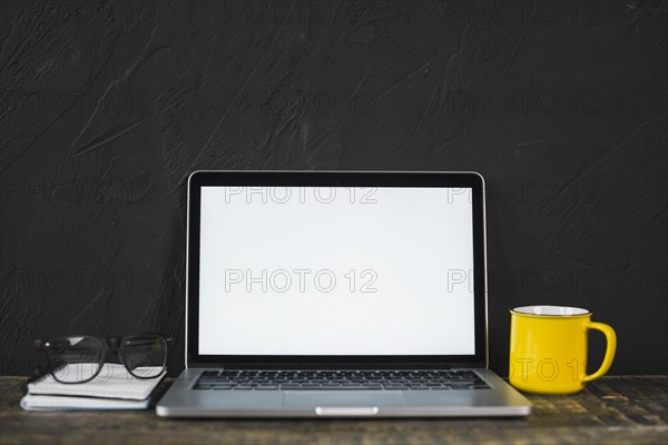 Laptop spectacle yellow coffee mug diary table with black textured wall