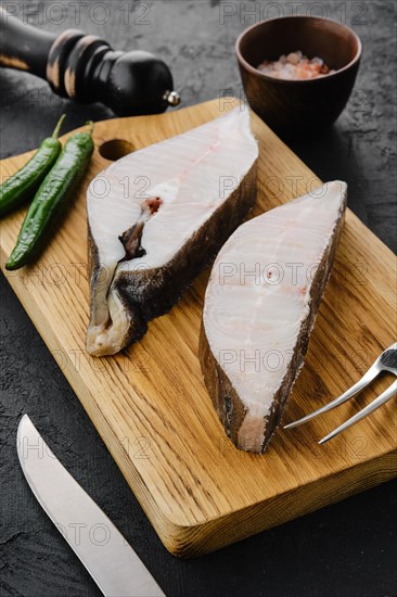 Closeup view of raw fresh halibut steak on wooden cutting board with spices