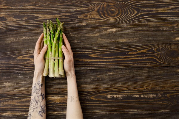 Overhead view of fresh asparagus in hand over wooden background