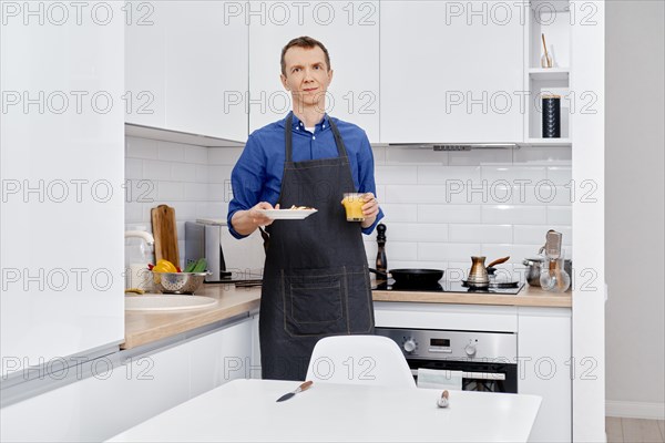 Middle age man brings plate with healthy food to the kitchen table
