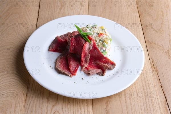 Roasted meat with salad olivier on wooden table