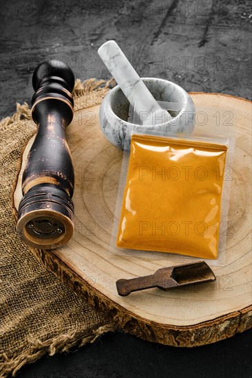 Wooden cross section with turmeric in plastic package and stone mortar and mill