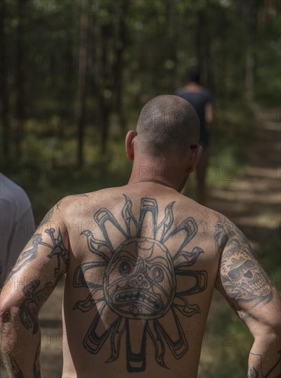 Man with tattoos on his back and arms walking through a forest