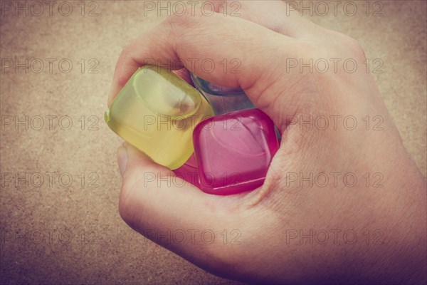 Hand holding fake colorful ice cubes on brown background