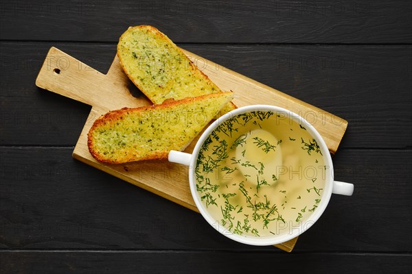 Top view of chicken stock with egg and crispy garlic toasted bread on wooden serving board