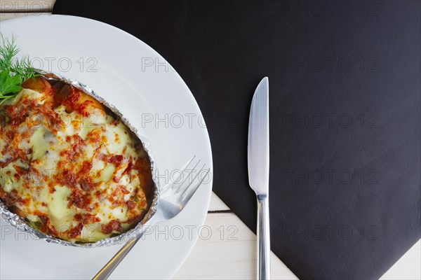 Top view of meat baked in foil with vegetables and cheese on wooden table