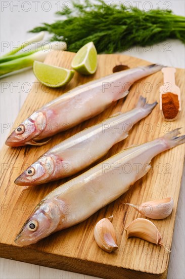 Raw fresh smelt fish on wooden cutting board with spice and herbs