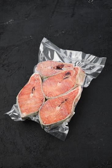 Overhead view of raw salmon steak in vacuum packaging on dark background