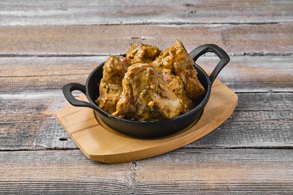 Lamb saddle marinated in mustard in cast iron skillet on wooden table