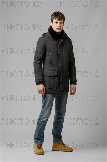 Full length portrait of handsome man in warm winter coat posing in studio
