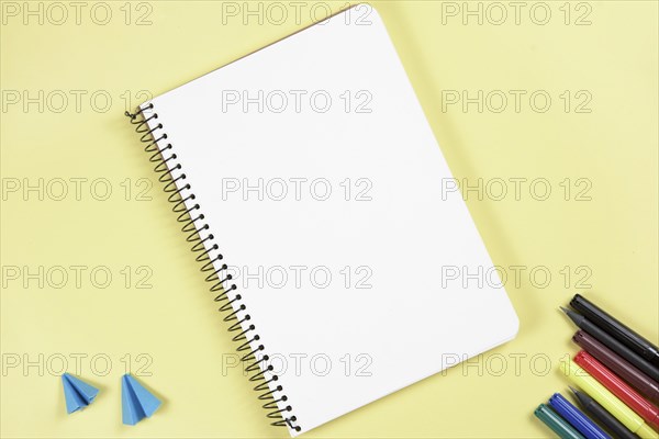 Folded craft paper felt tip pen near blank spiral notepad yellow background