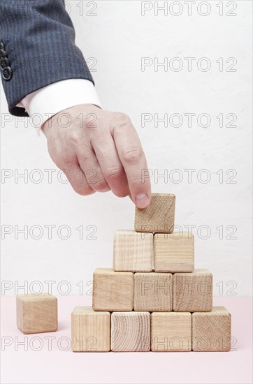 Hand creating pyramid from wooden cubes