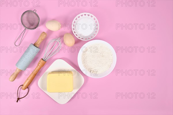 Cake dough ingredients and baking tools on pink background with copy space