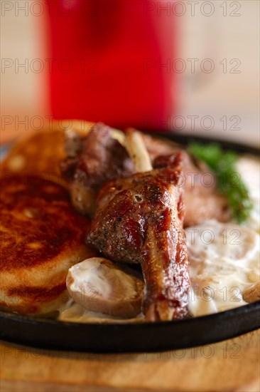 Fried in oven ribs with fritters and onion sauce. Cast iron pan on wooden cutting board and glass with cranberry juice