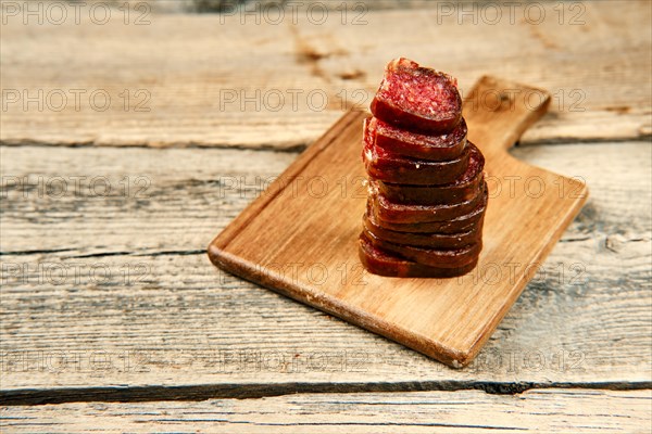Close up view of smoked dried stacked slices of deer and beef sausage on wooden cutting board