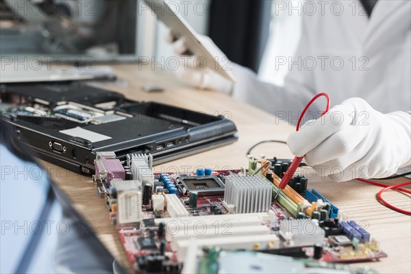 Male technician examining mother board with digital multimeter