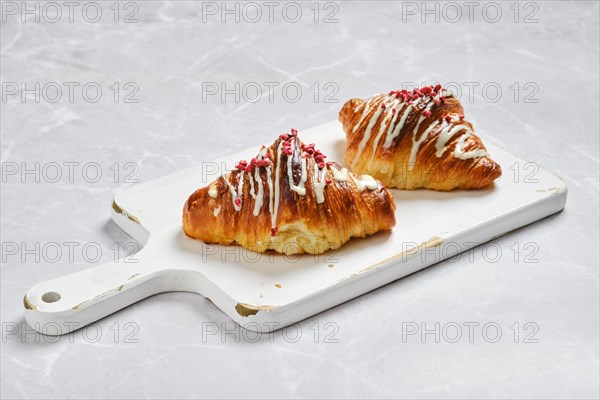 Two croissants with raspberry jam on white wooden board on marble background