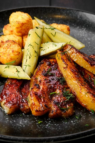 Closeup view of roasted pork belly with potato balls and pickled cucumber on a plate