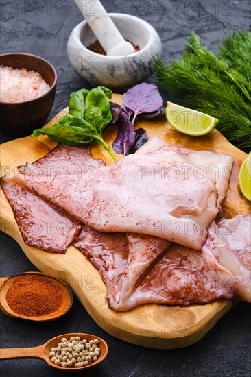 Raw fresh unpeeled squid on wooden cutting board with spice and herbs