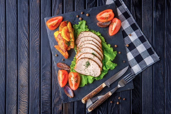 Sliced baked ham with fresh tomatoes on a stone plate in a rustic style