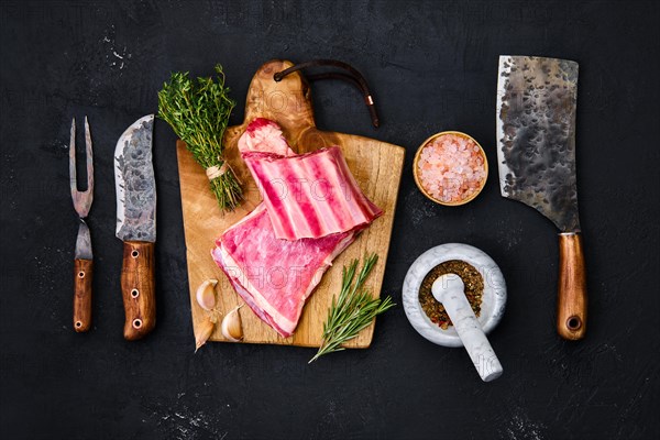 Fresh raw lamb breast ribs on wooden cutting board with herbs and seasoning