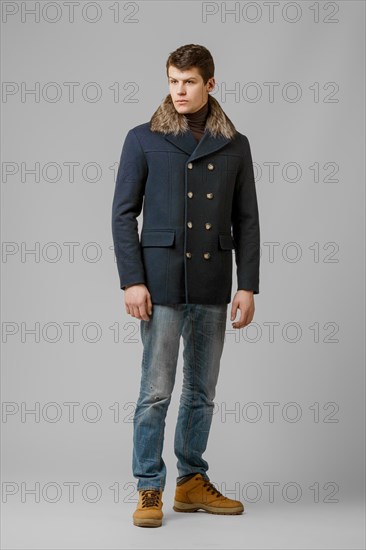 Full length portrait of handsome man in warm coat with hood posing in studio