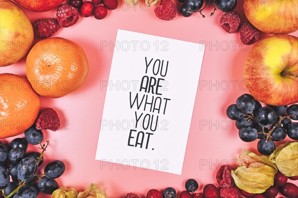 Healthy eating concept with You are what you eat card on pink background surrounded by fruits like apples