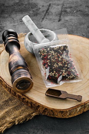 Wooden cross section with mixture of peppers in plastic package and stone mortar and mill