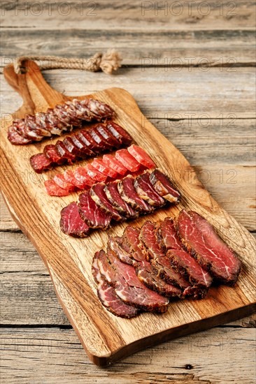 Slices of smoked dried beef and pork meat on wooden cutting board