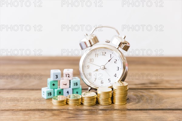 Close up stacked coins front alarm clock math blocks wooden desk