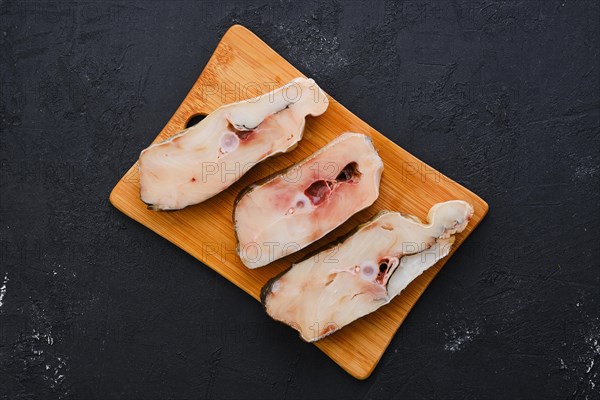 Top view of fresh raw cod steak on wooden cutting board with spice