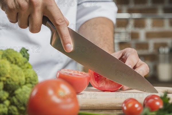 Chef s male hand cutting tomato with sharp knife board