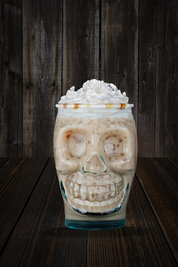 Halloween cocktail in goblet skull on wooden shelf. White monk drink in glass cup in the shape of skull