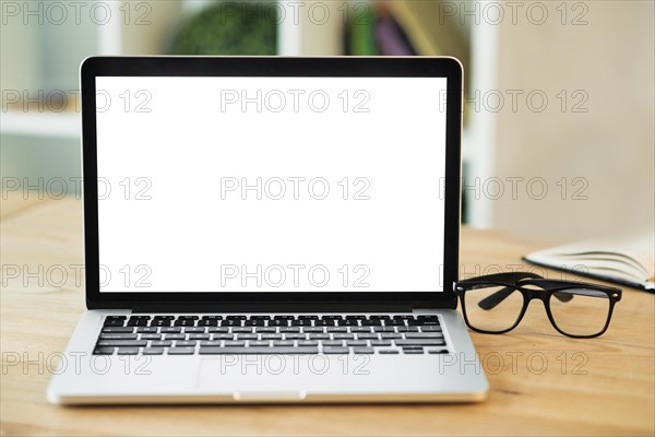 Laptop with blank white screen eyeglasses wooden desk