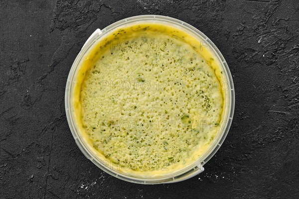 Top view of homemade soft cheese with herbs in plastic bowl