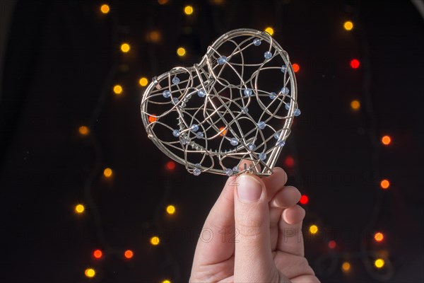 Heart shaped metal cage in hand on bokeh light background