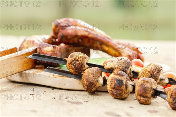 Grilled ribs and champignon on skewer served with fresh cucumber and tomato on wooden table outdoor