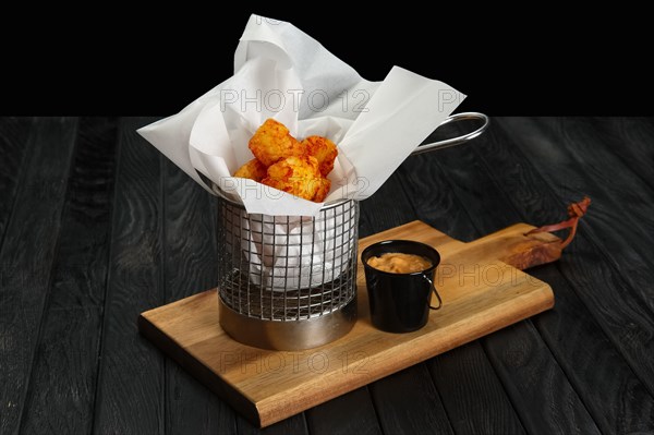 Deep fried potato balls in metal basket on wooden board