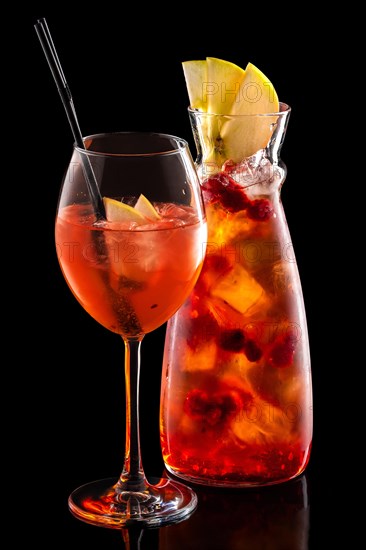 Cold sangria in pitcher and wine glass with ice cubes isolated on black background