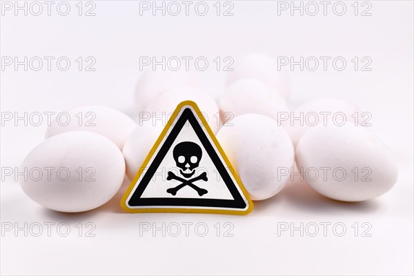 Concept for unhealthy or toxic substances in food like antibiotic residues or salmonella bacteria with skull warning sign on raw eggs on white background