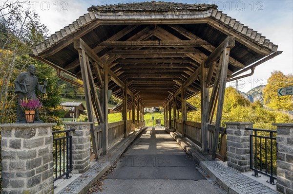 Wooden bridge over the Ostrach with Nepomuk statue in autumnal Ostrachtal