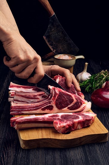 Chef cutting rack of lamb on wooden board. Preparing fresh meat for cooking