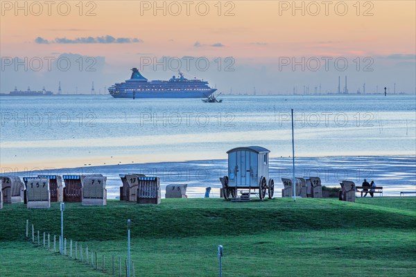 Grassy beach with beach chairs and cruise ship Artania on the Weser at dusk