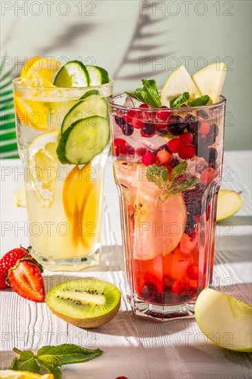 Variations of lemonades with different fruits and syrups on white wooden table under morning sun