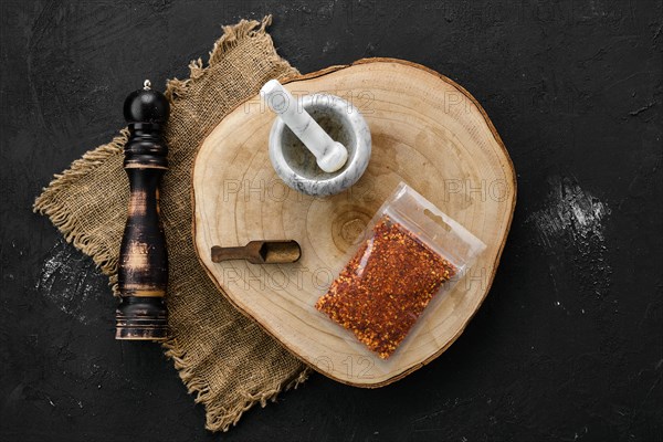 Wooden cross section with chili flakes in plastic package and stone mortar and mill