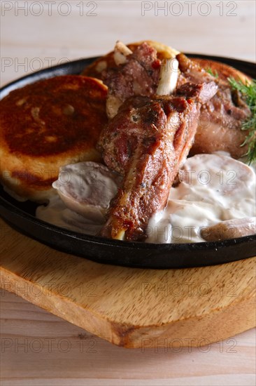 Fried in oven rabbit with fritters and onion sauce. Cast iron pan on wooden cutting board